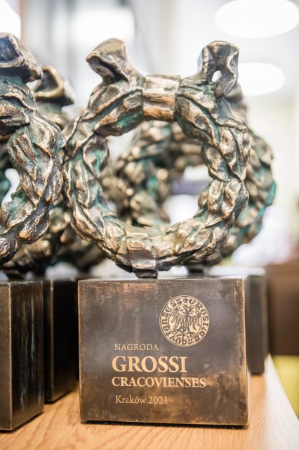 Nagrodą Grossi Cracovienses jest statuetka w kształcie wieńca wawrzynu. To bezpośrednie zapożyczenie dekoracyjnego motywu architektonicznego z bramy wejściowej do krakowskiej siedziby banku od strony ul. Basztowej. Jest to płaskorzeźba przedstawiająca wieniec ze splecionych liści wawrzynu, przepasany złotą wstęgą. Wawrzyn (inaczej laur) w formie wieńca był stosowany jako motyw zdobniczy w sztuce i architekturze już od czasów starożytnych. Będąc nagrodą zwycięstwa, jest interpretowany jako symbol sukcesu.